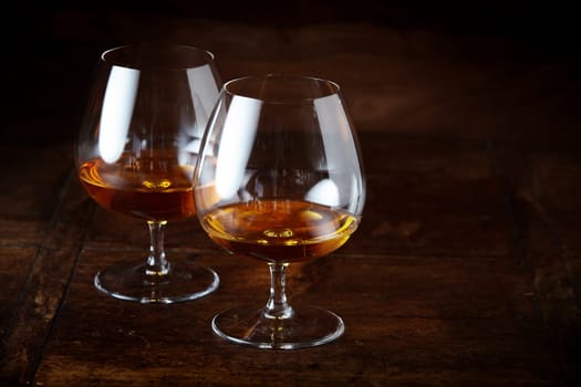 Two cognac snifter glasses with beverage, viewed in close-up from high angle against dark brown counter surface with copy space