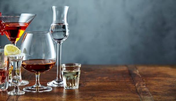 Assorted alcoholic beverages on rustic bar counter with copy space over textured slate behind in a panorama banner