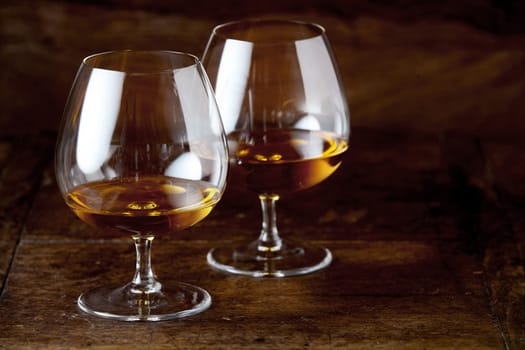 Two brandy snifter glasses with cognac in close-up on dark brown wooden counter surface with copy space