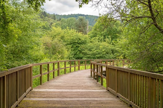 Bridge made of wooden boards over a green field with trees and wooded hills