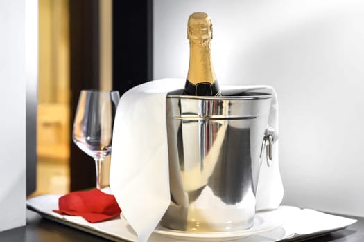 Bottle of cold wine or champagne in ice bucket on white table at hotel room. Wedding reception, holiday concept. Copy space.