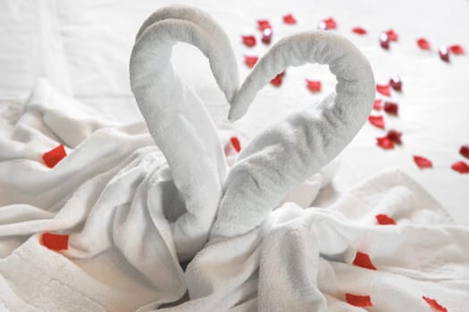 White two towel swans on the bed, sprinkled with red petals. The towel look like heart shape and it's prepare for couple in honey moon. Ideal for events and concepts.