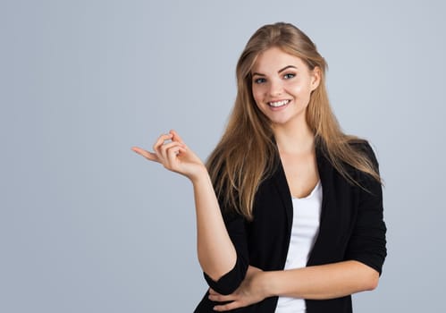 Blonde girl pointing aside, isolated on grey