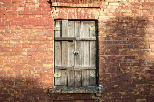 Old wooden window with closed shutters on red brick wall.