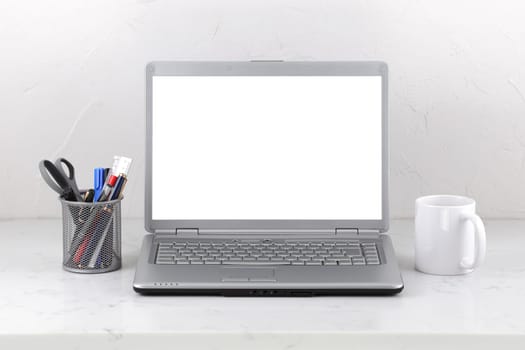 A laptop on marble office desk coffee mug and pens. White screen template with clipping path