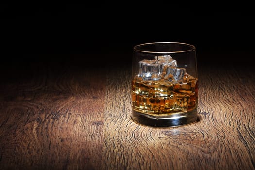 A Scotch in glass tumbler with ice rocks on old wood surface