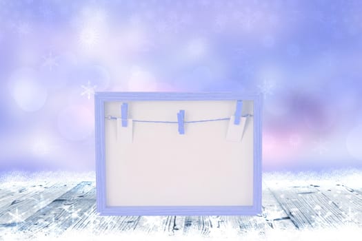 Empty pink wooden frame with a clothesline and clothespins on a rustic wooden table with snow over abstract winter christmas or other holidays background. Space for design. Card concept.