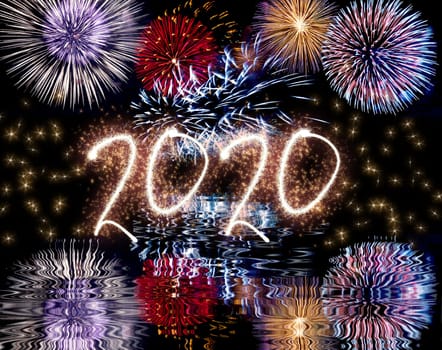Colorful fireworks in the night sky with reflect in water and sparkling 2020 text