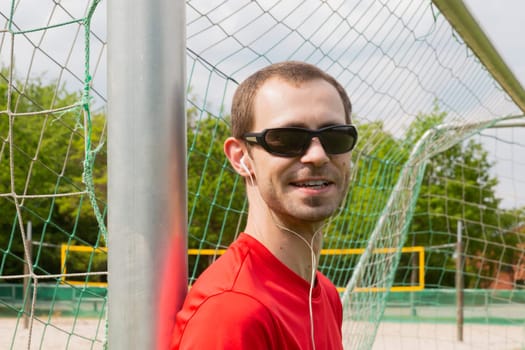 Friendly young sportsman with sunglass and earphones outdoor in a park