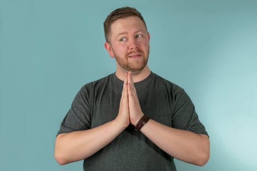 Half body portrait of young man with hands together in prayer looking to side, studio background.