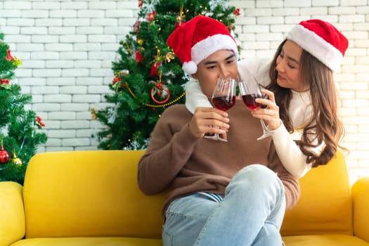Young asian adult teenager couple celebrateing christmas holiday with wine together in living room with christmas tree decoration.