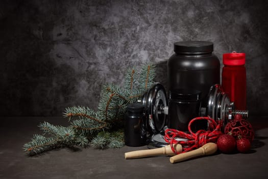 Sports nutrition (supplements), dumbbell, bottle for water, jump rope and Christmas ornaments on dark grey background with copy space. Fitness, sport or healthy lifestyle concept. New Year. Christmas.