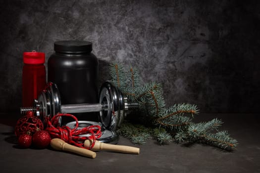 Sports nutrition (supplements), dumbbell, bottle for water, jump rope and Christmas ornaments on dark grey background with copy space. Fitness, sport or healthy lifestyle concept. New Year. Christmas.