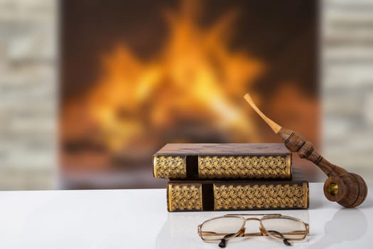 Winter christmas books background. Two old books with a tobacco pipe on them and a reading glasses on a table in front of abstract blurred fireplace. Reading books in holiday time. Space.