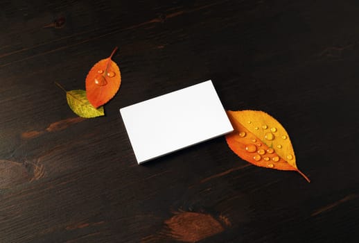 Blank business card and autumn leaves on wooden background. Responsive design mockup.