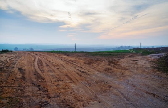Dirty gravel road in the countryside. Evening rural landscape.