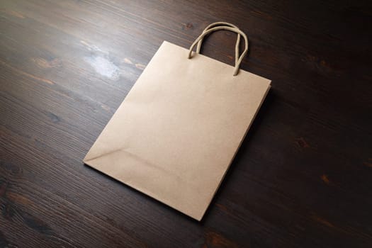 Blank disposable paper bag with rope handles on wood table background.
