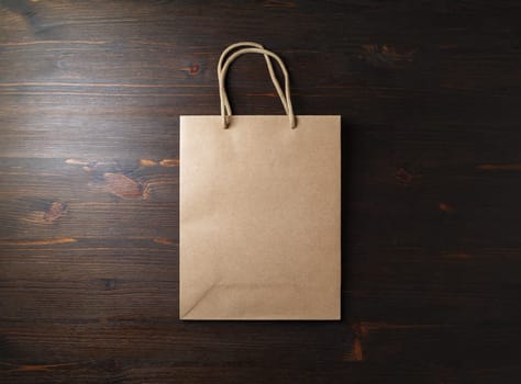 Blank brown paper bag with rope handles on wooden background. Flat lay.