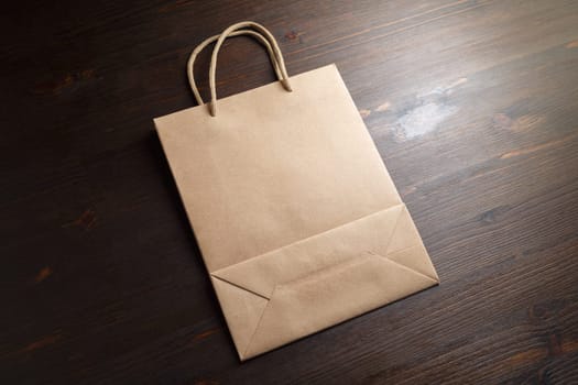 Blank brown paper shopping bag with rope handles on wooden background.