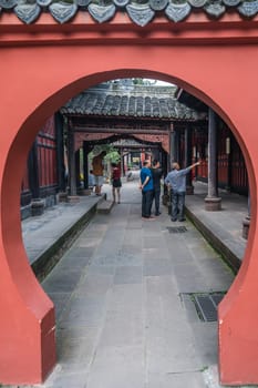 Chengdu, China -  July 2019 : Rounded moongate view of pilgrims or tourists standing in the lengthy corridor in the courtyard of the 17th century Buddhist Wenshu Monastery temple, Chengdu, Sichuan Province