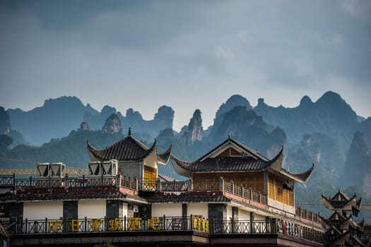 Wulingyuan, China - August 2019 : Rooftops of traditional chinese buildings with the stunningly beautiful rocky karst mountain formations behind as seen from the centre of town, Hunan Province