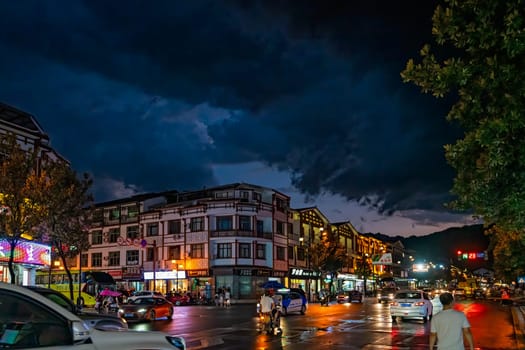 Wulingyuan, China - August 2019 : Bustling life with cars, traffic and lights on buildings lit at night at a busy high street in Wulingyuan town at dusk