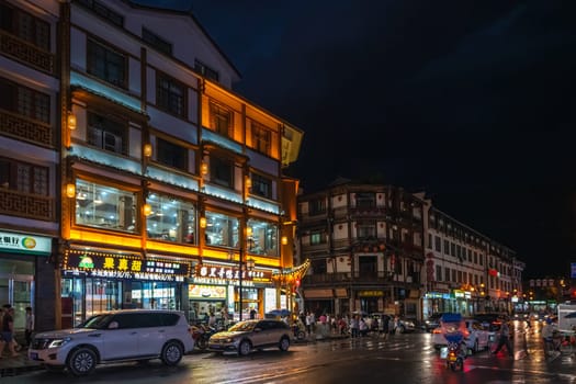 Wulingyuan, China - August 2019 : Bustling life with cars, traffic and lights on buildings lit at night at a busy high street in Wulingyuan town at dusk