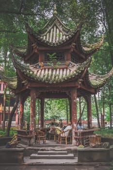 Chengdu, China -  July 2019 : Older senior people sitting on wicker chairs under pagoda roof and relaxing in the Chinese garden in the Wenshu Monastery, Sichuan Province