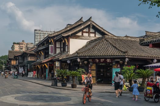 Chengdu, China -  July 2019 : Street scene in the city of Chengdu in summer, woman riding on her bicycle with old traditional chinese buildings in the background, Sichuan Province