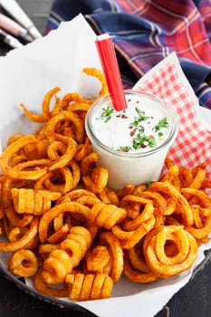 Basket full of crunchy curly fries with a jar of dip
