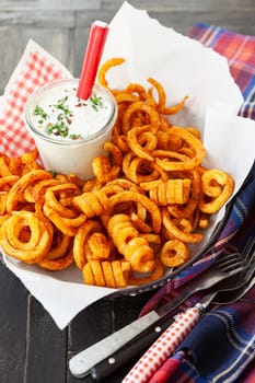 Basket full of crunchy curly fries with a jar of dip