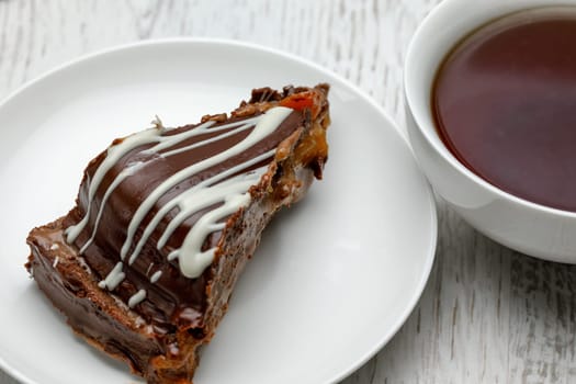 Homemade chocolate cake with chocolate glaze with white stripes on brown and a cup of tea