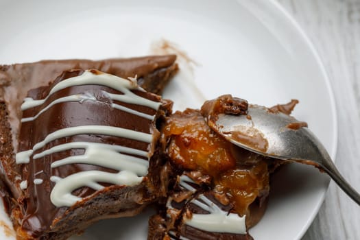 Broken piece of chocolate homemade cake with apricot jam and a spoon