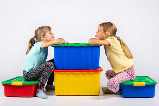 Two girls sit on big boxes for toys and show each other tongue