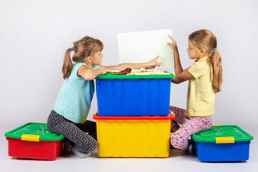 Two girls sit on large toy boxes and look at the toy assembly instructions