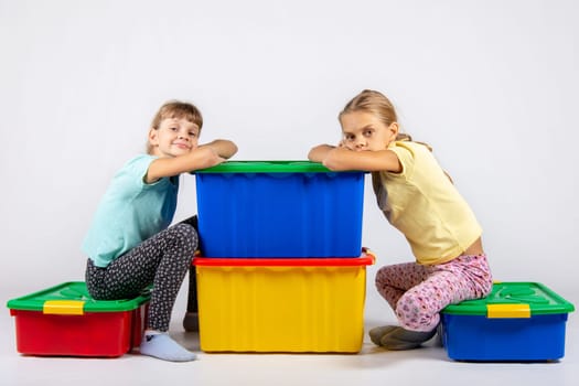 Two girls are sitting on large boxes for toys and looked into the frame