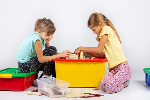 Two girls are assembling a house on a box with toys, looking in the instructions
