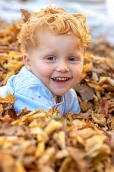 Portrait of happy little red hair boy lying in the middle of colorful autumn leaves