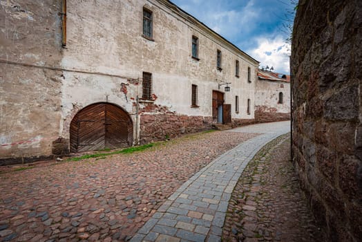 Courtyard of Vyborg castle in Russia. Old street with pathway and cobblestone floor. Blue cloudy sky in background.