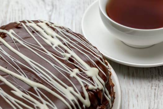 Homemade chocolate cake with chocolate glaze with white stripes on brown and a cup of tea