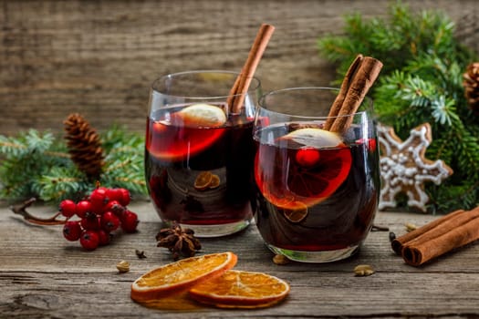 Mulled wine in glasses in a Christmas setting with dry slices of oranges, cookies in the shape of a snowflake, red berries and cinnamon