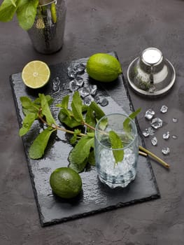 bar tool: cocktail shaker and glass with ice, lime and mint on dark stone table. Top view. Bartender's tool. Mojito cocktail making.