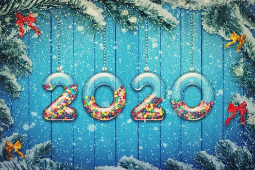 Happy New Year 2020 holiday background. Set of transparent numbers made of glass filled with multicolored candy and sweets hang on snowy Christmas tree branches.