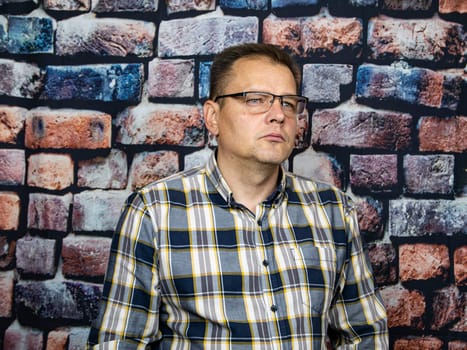 A man with glasses on a brick wall background. People.