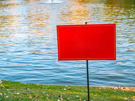 Red warning sign on the shore of a pond. Place for text.