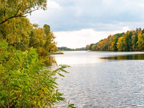 Autumn river landscape against a cloudy sky. Autumn foliage. Water. Background image. River bank.