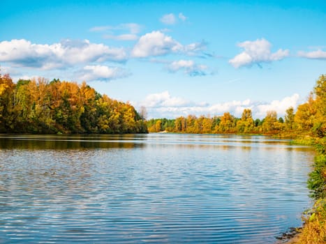 Autumn river landscape against a cloudy sky. Autumn foliage. Water. Background image. River bank.