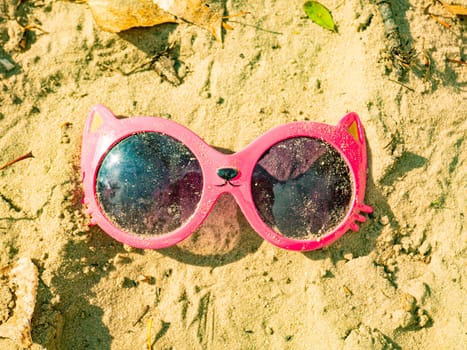 Baby pink sunglasses are in the sand. Girls. Children's games.