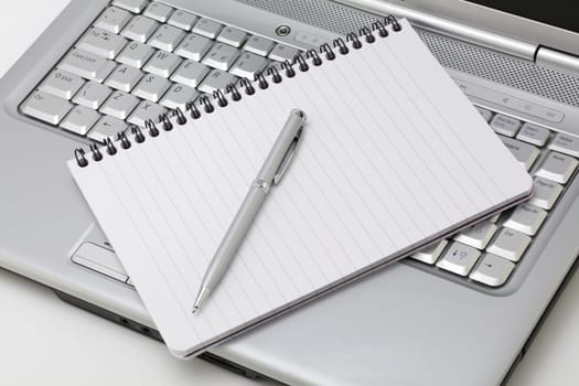 A notebook and pen resting on a laptop PC