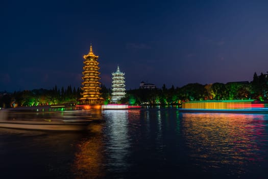 Tourist boats sailing in front of illuminated at night Sun and Moon Pagodas Towers at Shanhu or Shan Lake in Guilin town, Guangxi Province, China